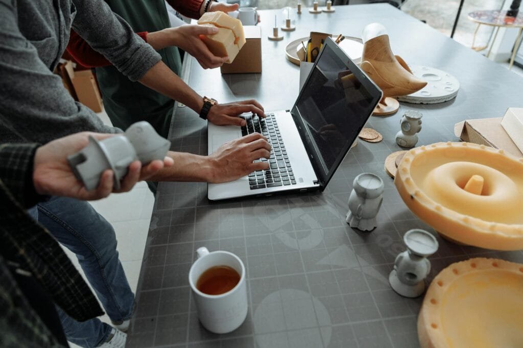 People Standing Beside Man Using Laptop on Gray Table with Silicon Forms